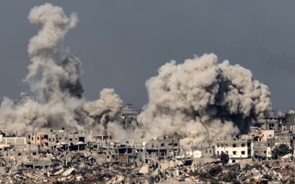 A picture taken from southern Israel near the border with the Gaza Strip on 8 December, 2023, shows smoke rising above buildings during an Israeli strike in northern Gaza, amid continuing battles between Israel and the militant group Hamas.