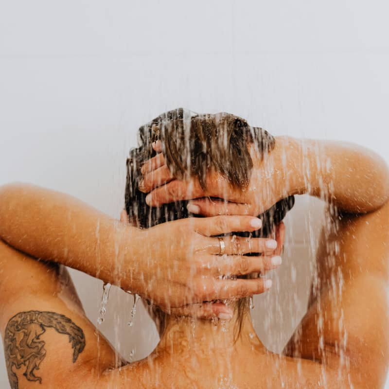 A woman washes the back of her neck in the shower.