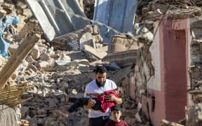 A man carries a boy as he walks past destroyed houses after the earthquake, in the mountain village of Tafeghaghte, southwest of Marrakesh, on 9 September, 2023.
