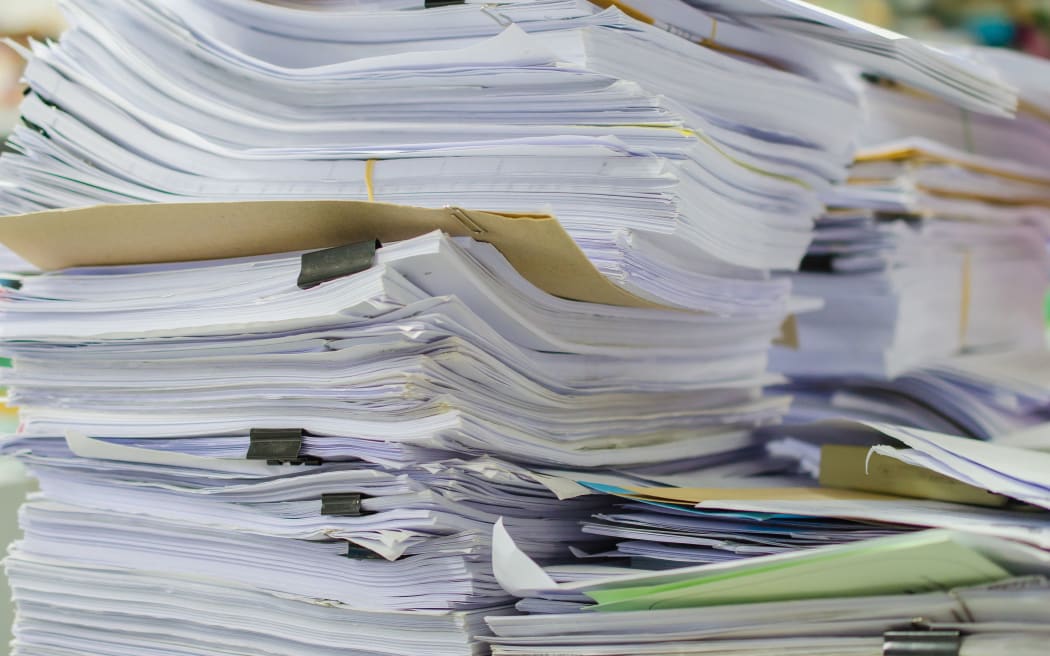Pile of documents on desk stack up high waiting to be managed.