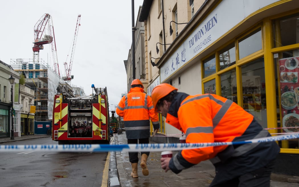 Workmen enter a restricted area closed by police after a crane bent overnight in high winds brought by Storm Katie in south London.