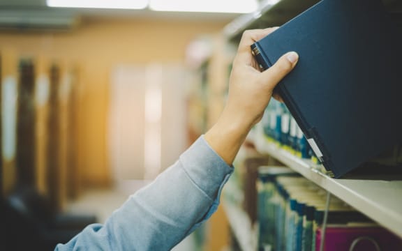 Close-up of hand picking up book on bookshelf in library to go to study.back to school concept