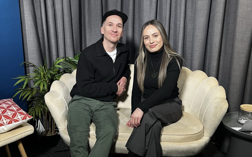 Te reo Māori advocate and kaiako Hēmi Kelly sits on a cream couch with The TAHI podcast's Waimirirangi Lee-Reiri smiling at the camera