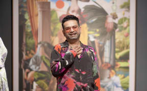 Pranay stands in front of a work of art at a gallery. He wears a shirt with a graphic design across it. He smiles openly.