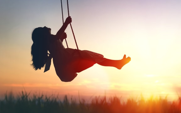 Happy laughing child girl on swing in sunset summer.