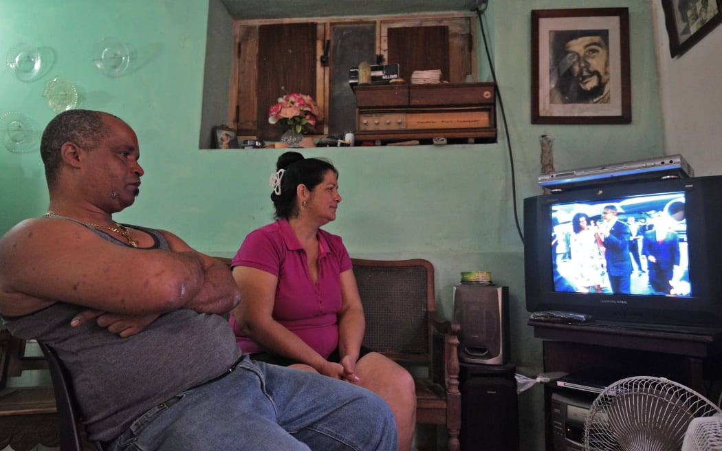 A Cuban family in Havana, with a photo of legendary Argentine-Cuban revolutionary Ernesto "Che" Guevara on the wall, watch on TV the arrival of US President Barack Obama to Cuba on March 20, 2016.