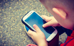 Little boy child kid playing games on smartphone mobile phone outdoor. Technology generation.