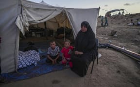 A Palestinian woman sits in front of her makeshift tent with her grandchildren after been displaced by the Israeli air and ground offensive on the Gaza Strip at a camp in Deir al Balah, on13 May, 2024.