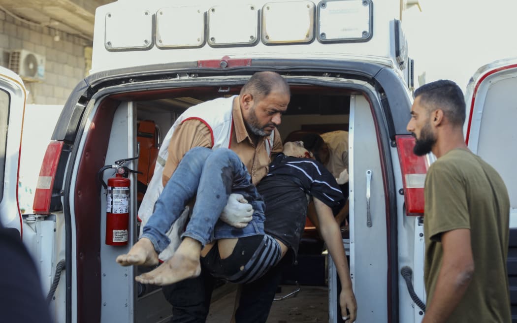 A man carries a wounded child into an ambulance following airstrikes in the Nuseirat refugee camp in central Gaza on October 19, 2025. The incident followed Israeli airstrikes across the Gaza Strip, reported after the breakdown of a recent ceasefire. (Photo by Ahmed Younis / Middle East Images via AFP)