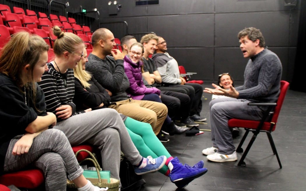 An actor sitting in a chair in front of a small audience that is laughing