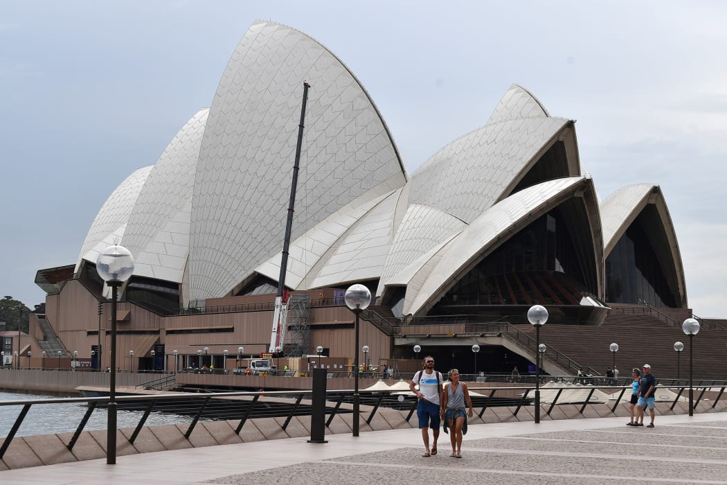 A few people walk along Circular Quay outside the Opera House in Sydney on March 25, 2020, as people stay away due to restrictions to stop the spread of the worldwide COVID-19 coronavirus outbreak.