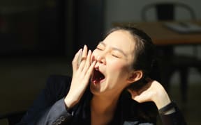 An Asian woman yawning at her desk.