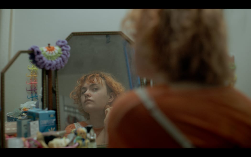 Finn Hitch (They/Them) applying makeup in front of their bedroom mirror
