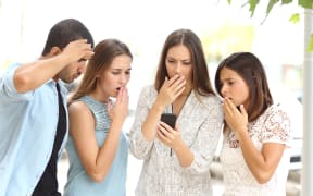 A photo of four worried multi ethnic friends watching a smart phone in the street