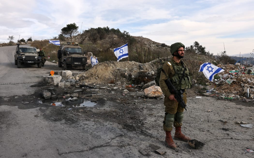(FILES) In this file photo taken on December 30, 2021 Israeli soldiers guard the road leading to the Homesh Yeshiva (religious school), located at the former settlement of Homesh, west of the West Bank city of Nablus. - Israel's settler movement won a victory in the parliament on March 21, 2023 by overturning  a law banning them from residing in areas of the northern West Bank from which Jewish settlers were evacuated in 2005. (Photo by MENAHEM KAHANA / AFP)