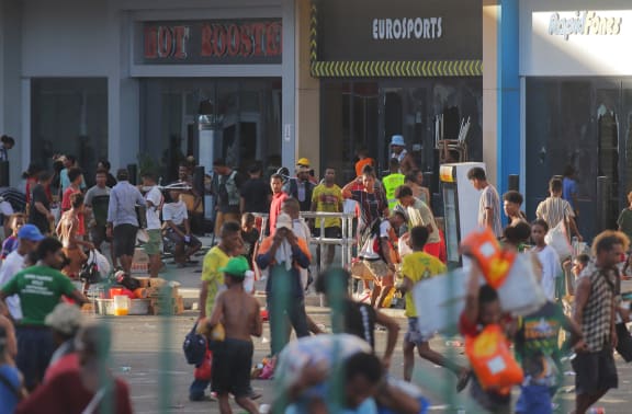People carry items as crowds leave shops with looted goods amid a state of unrest in Port Moresby on January 10, 2024. Papua New Guinea's prime minister declared a 14-day state of emergency in the capital on January 11, 2024, after 15 people were killed in riots as crowds looted and burned shops. (Photo by STRINGER / AFP)