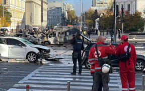 A video grab taken from an AFPTV footage shows vehicles destroyed in Kyiv on 10 October 2022. Security and emergency personnel work at the scene after several missile strikes were heard in the Ukrainian capital.