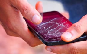 Image of a two hands holding a mobile phone with a broken screen.