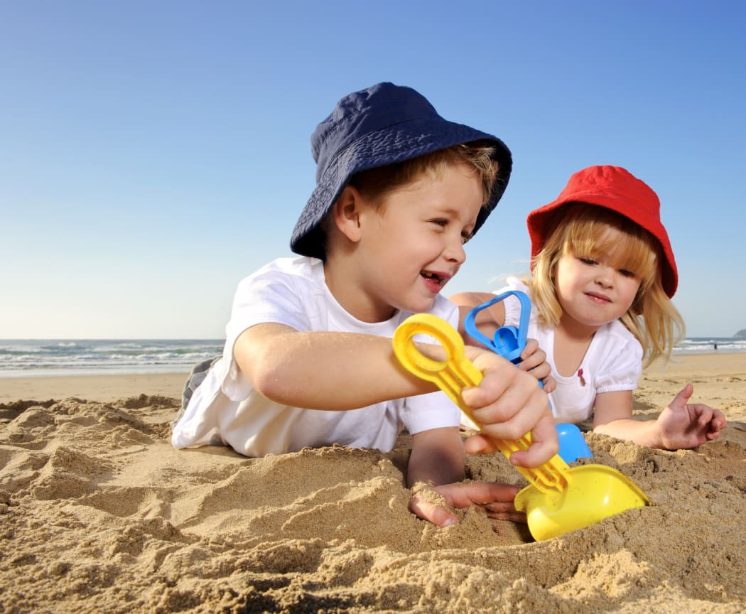 Two children wearing hats play with spades on a sunny day at the beach.