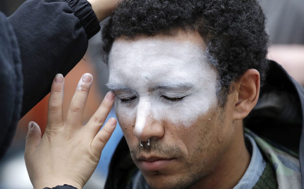 FILE - In this Oct. 31, 2018, file photo, a man, who declined to be identified, has his face painted to represent efforts to defeat facial recognition during a protest at Amazon headquarters over the company's facial recognition system, "Rekognition," in Seattle.