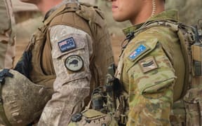Close up of New Zealand and Australian soldiers side by side in uniform with their country flag on their sleeves.