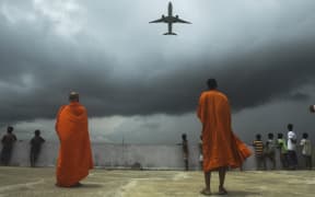 Buddhists monks and children look out from the rooftop at a Buddhist mission hostel and school for underprivileged children as an international passenger flight takes off from Kolkata, India.