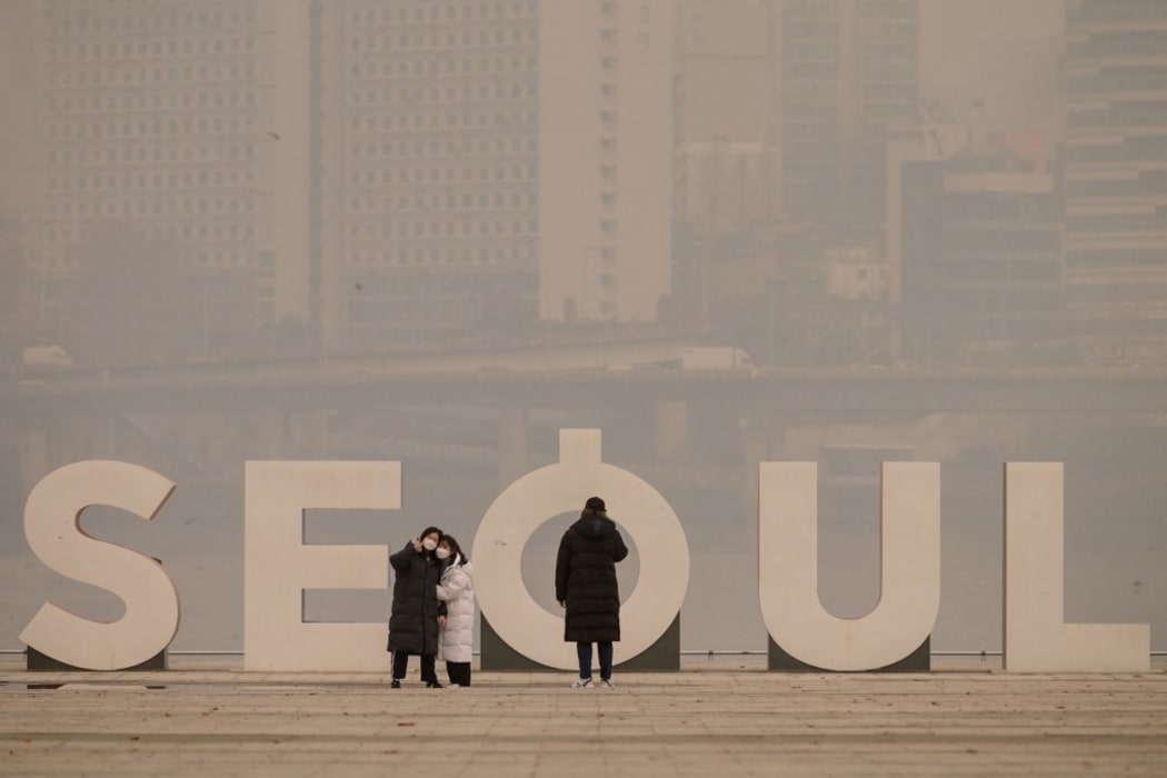 People wearing face masks take photos in front of the city skyline during heavily polluted weather conditions in Seoul on December 10, 2019. - According to the World Air Quality Index, levels of ultra-fine particuate matter reached 194 in South Korea.
