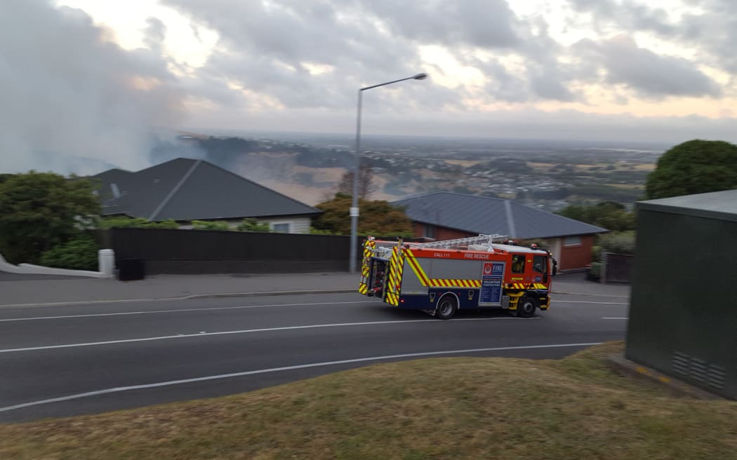 A fire engine speeds through Christchurch as smoke billows from the Port Hills fire.