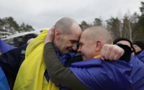 In this handout photograph released by the Telegram account of Ukraine's President Volodymyr Zelensky on March 5, 2026, repatriated Ukranian servicemen wrapped in national flags embrace after they were released during a prisoner swap at an undisclosed location. Moscow and Kyiv will each release a total of 500 prisoners of war over March 5 and 6, 2026, Russia's top negotiator said, with the Russian defence ministry saying the first 200 on each side had already been swapped.