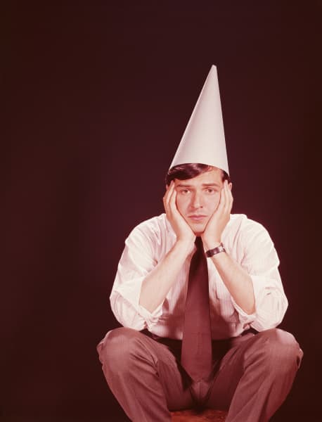 An 1970s style image of a salaryman in office attire sitting with hands in head and wearing a party hat.