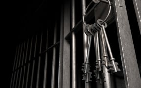 A closeup of the lock of a  jail cell with iron bars and a bunch of key in the locking mechanism with the door open