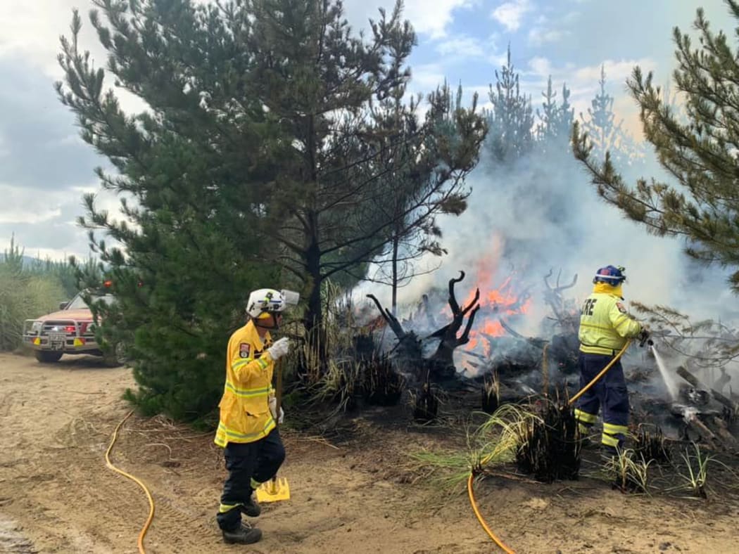 Muriwai Volunteer Fire Brigade firefighters tackling a forest fire which started from a campfire at Muriwai Beach.