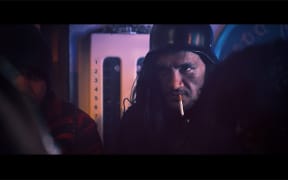 Long-haired Māori man wearing an army helmet with a cigarette hanging out of his mouth