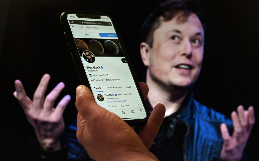 (FILES) In this file illustration photo taken on April 14, 2022 a phone screen displays the Twitter account of Elon Musk with a photo of him shown in the background, in Washington, DC. - Tesla boss Elon Musk's road to turning Twitter into a money-making platform where anyone can say anything looks to experts like a tough one. Musk's $44-billion deal to buy the global messaging platform must still get the backing of shareholders and regulators. (Photo by Olivier DOULIERY / AFP)