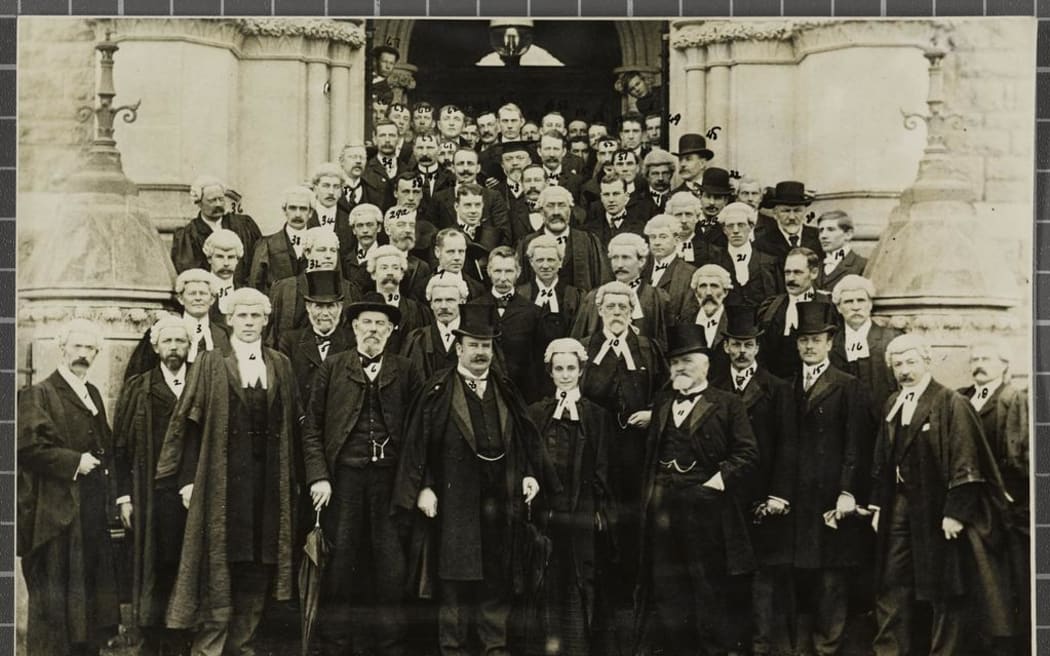 A large group of lawyers standing on the front steps of the Dunedin Law Courts, with Sir Joseph Ward and Ethel Benjamin in the centre at the front. Most of the people are numbered and there is a key to the names housed with the photograph. 1902.