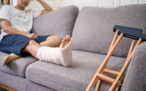 Young Asian man with a broken leg sitting on the sofa. Close up of the crutch.