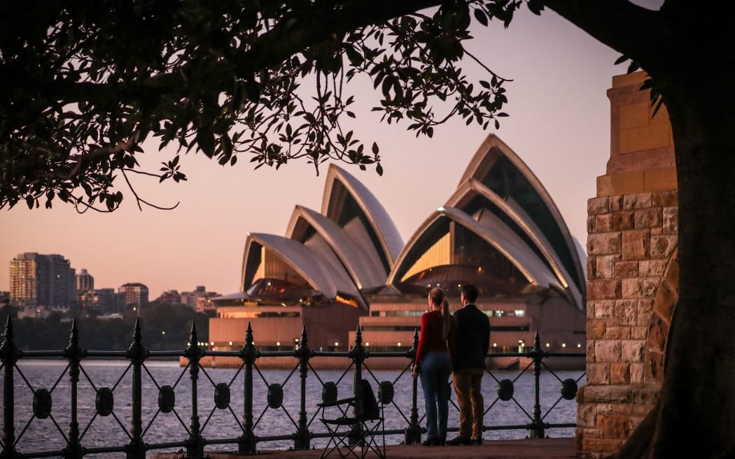 Residents observe a moment of silence at dawn in front of the Opera House in Sydney on April 25, 2020. - Australians and New Zealanders stood outside their homes across the country at dawn on April 25 to honour their war dead after the Covid-19 lockdown forced the cancellation of traditional remembrance day services. (Photo by DAVID GRAY / AFP)