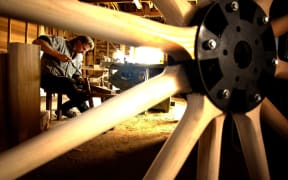 Man in workshop woodworking in a photo shot through the spokes of a wooden wheel