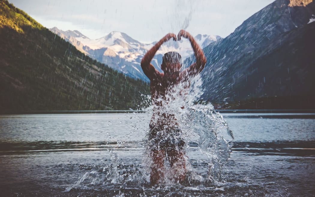The guy bathed in a cold mountain lake in the evening at sunset. Water splashes on the lake.