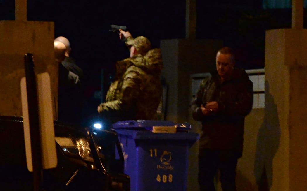A police officer holds a gun over the front gate of a residential area in the Melbourne bayside suburb of Brighton during the siege.
