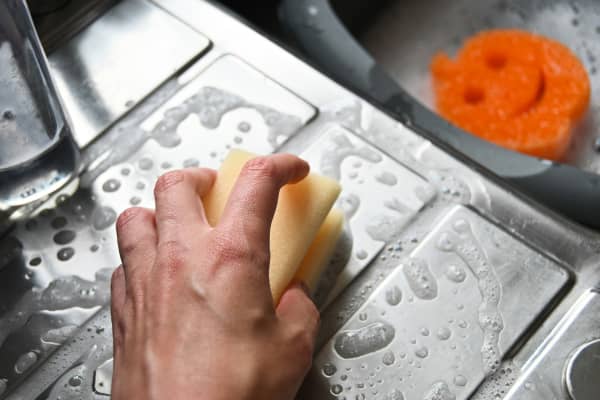 A close-up of a hand holding a foamy sponge, scrubbing a kitchen sink.