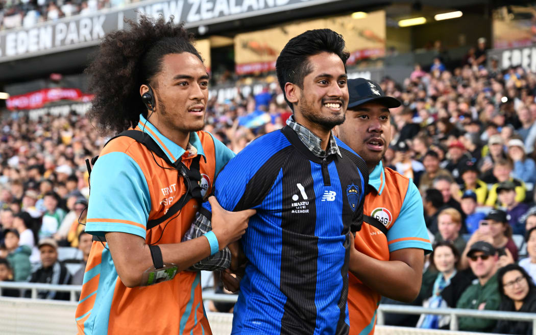 Security removes a pitch invader in an Auckland FC shirt during the Wellington Phoenix v Sydney FC. A-League football match at Eden Park.