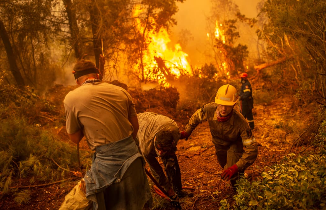 Firefighter and volunteers use a water hose near a burning blaze trying to extinguish a fire in the village of Glatsona on Evia island.