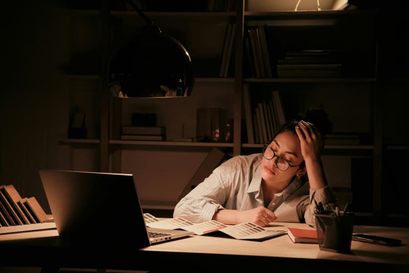 A picture of a woman who is working late at night, in front of a laptop, and exhausted.