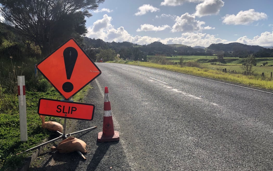 An orange road warning sign saying 'slip'. The road is in a rural area.
