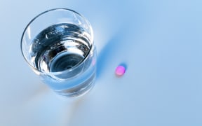 A pink pill next to a glass of water (stock photo)