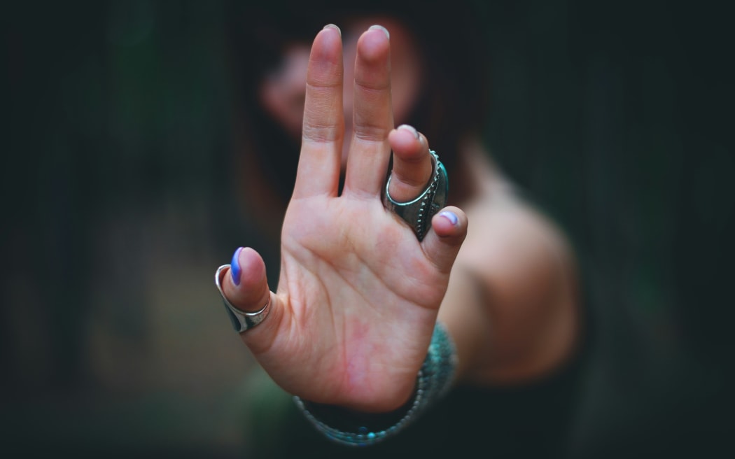 A woman holds her hand in the air in a blocking gesture.