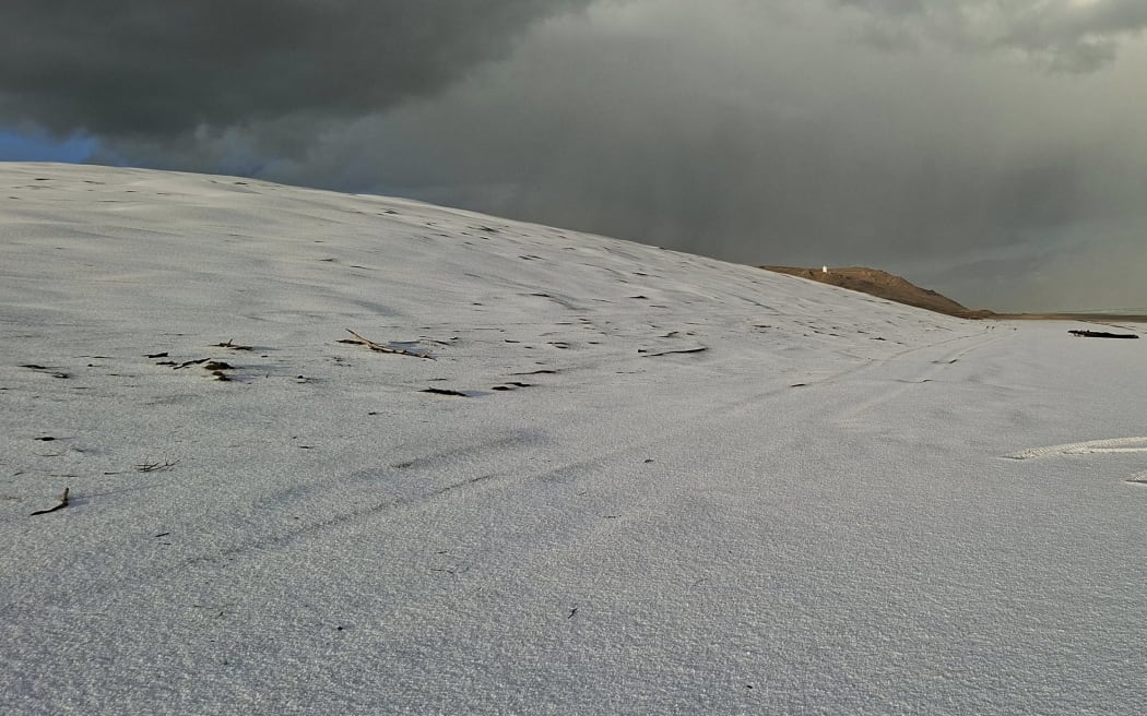 The beach at Pouto, south of Dargaville, is blanketed in ice after a freak hail storm. 
Pouto Point lighthouse in the distance.