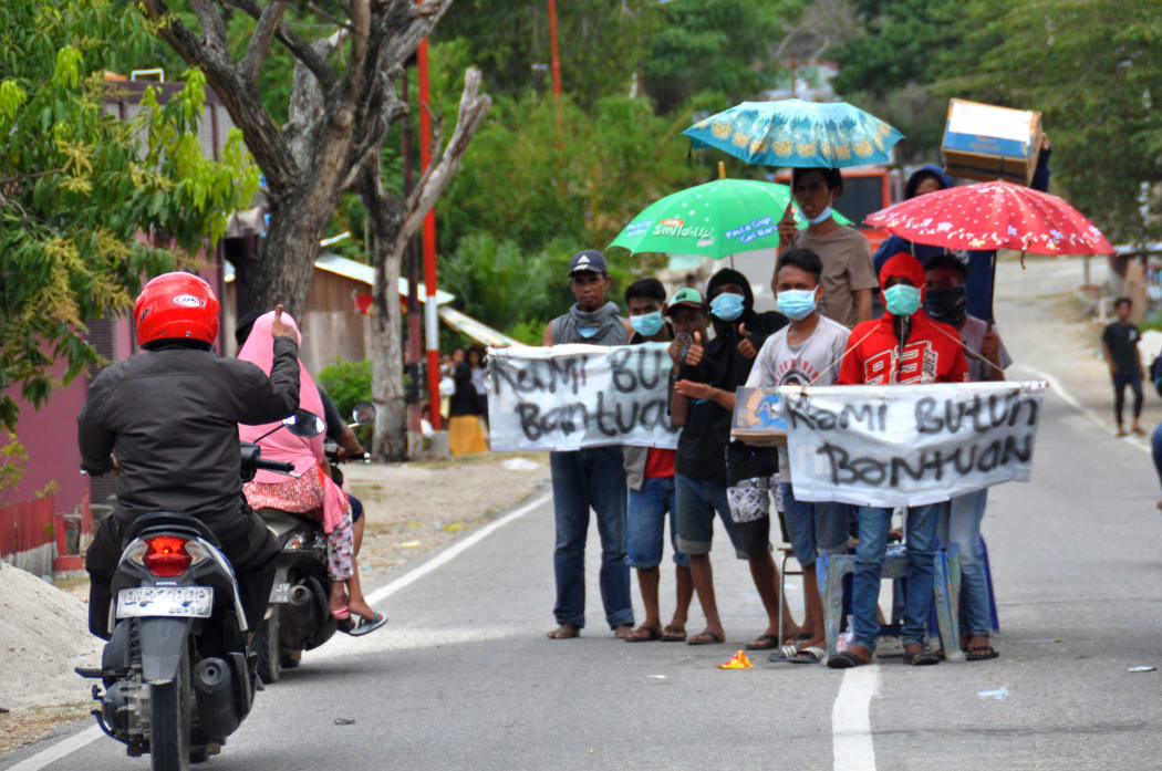 A group of villagers hold placards along a road near their destroyed village, asking for assistance in Palu, Indonesia's Central Sulawesi.