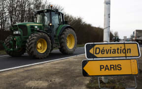 A French farmer drives a tractor next to a sign reading "Diversion to Paris" as they arrive at Chambly, some seventy kilometers from the north of Paris, on January 29, 2024, amid nationwide protests called by several farmers unions on pay, tax and regulations. Local branches of major farmer unions FNSEA and Jeunes Agriculteurs announced on January 27, 2024, a "siege of the capital for an indefinite period" starting at 2 p.m. on January 29, 2024, as some farmers feel that the government's announcements in favor of the sector are insufficient. (Photo by Sameer Al-Doumy / AFP)